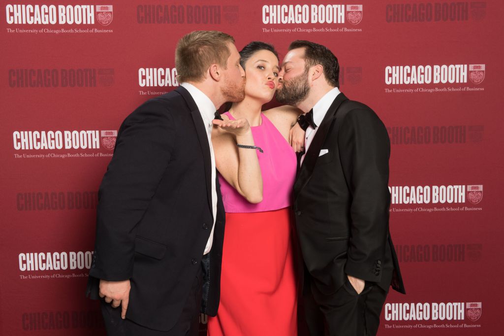 Men give lady kiss on both cheeks on step repeat photo activity for Chicago Booth